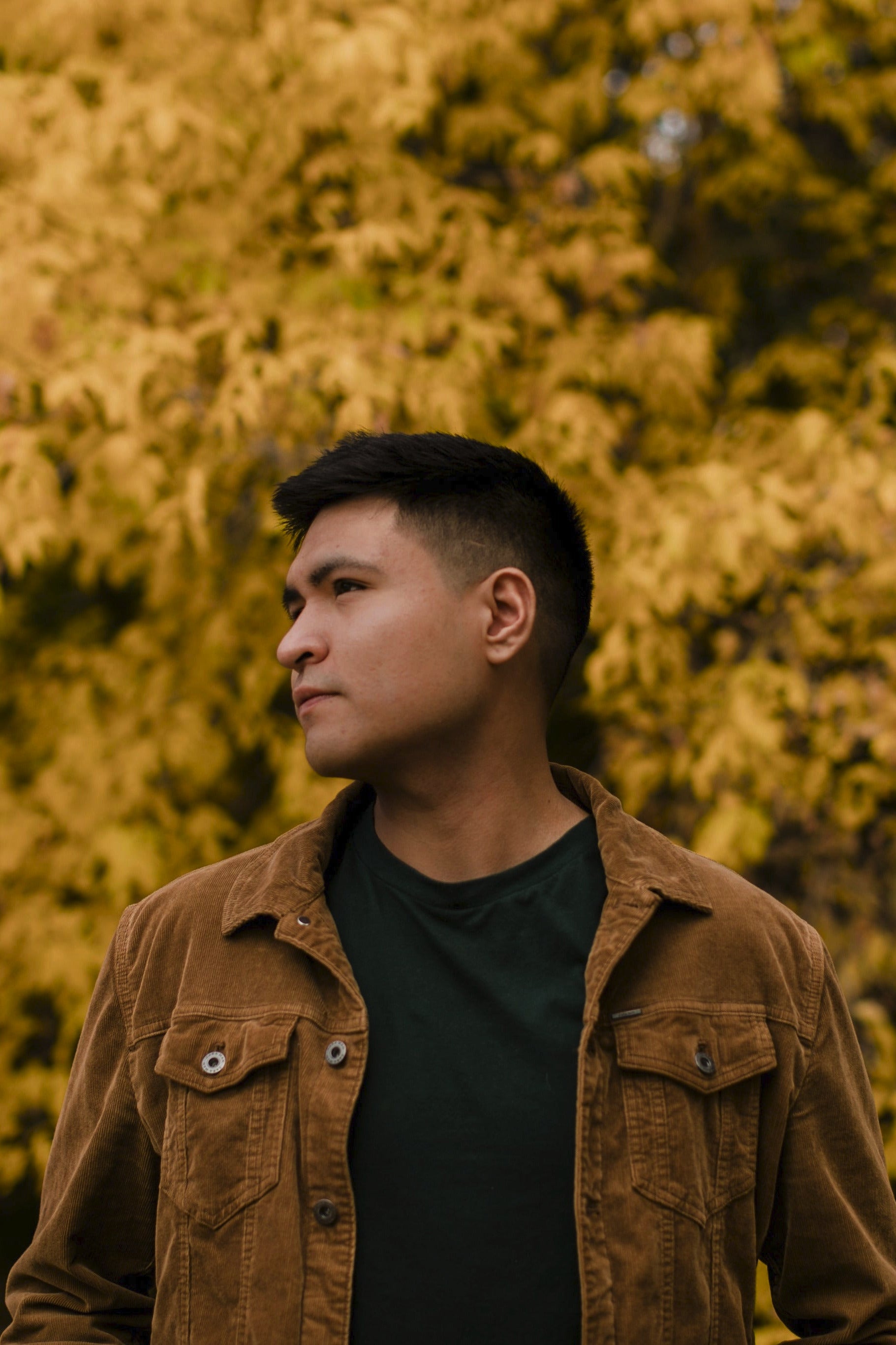 Man wearing a brown jacket standing in front of a blurred natural background